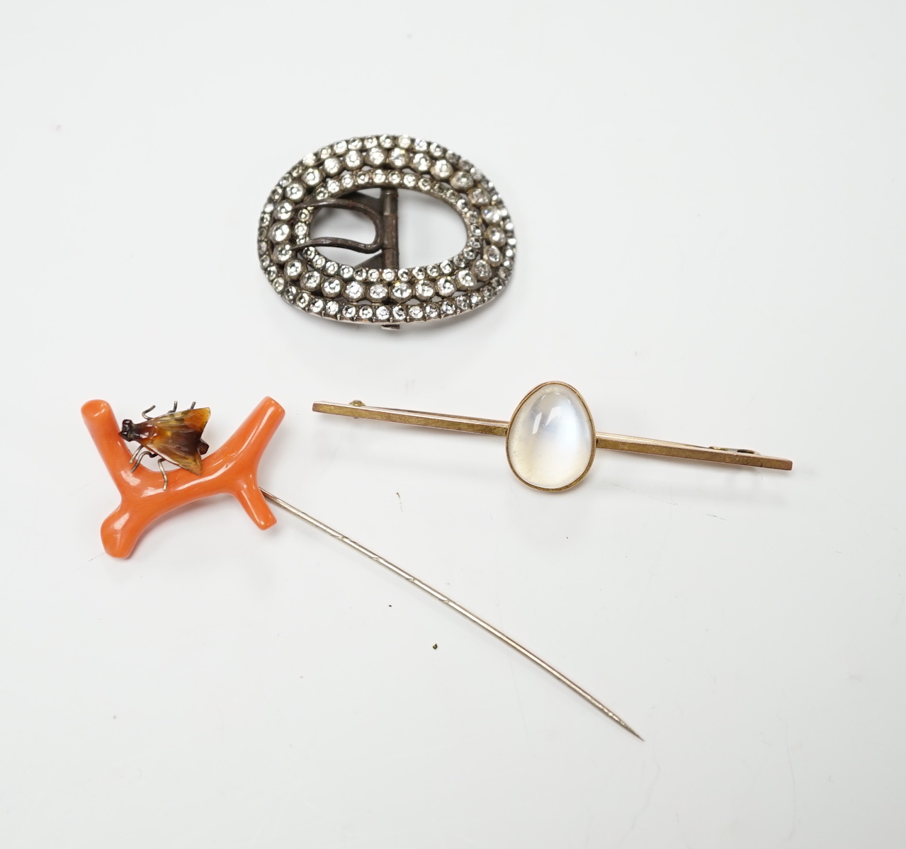 A 9ct and cabochon moonstone set bar brooch, 63mm, a coral and horn set bug stick pin and a paste set buckle.